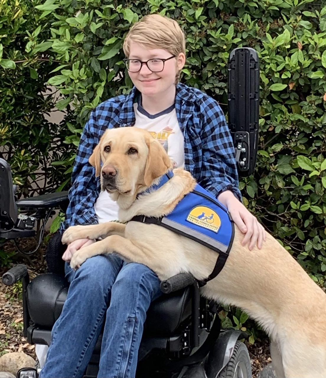 Izzy smiling with Maeve, their Canine Companions service dog, on their lap